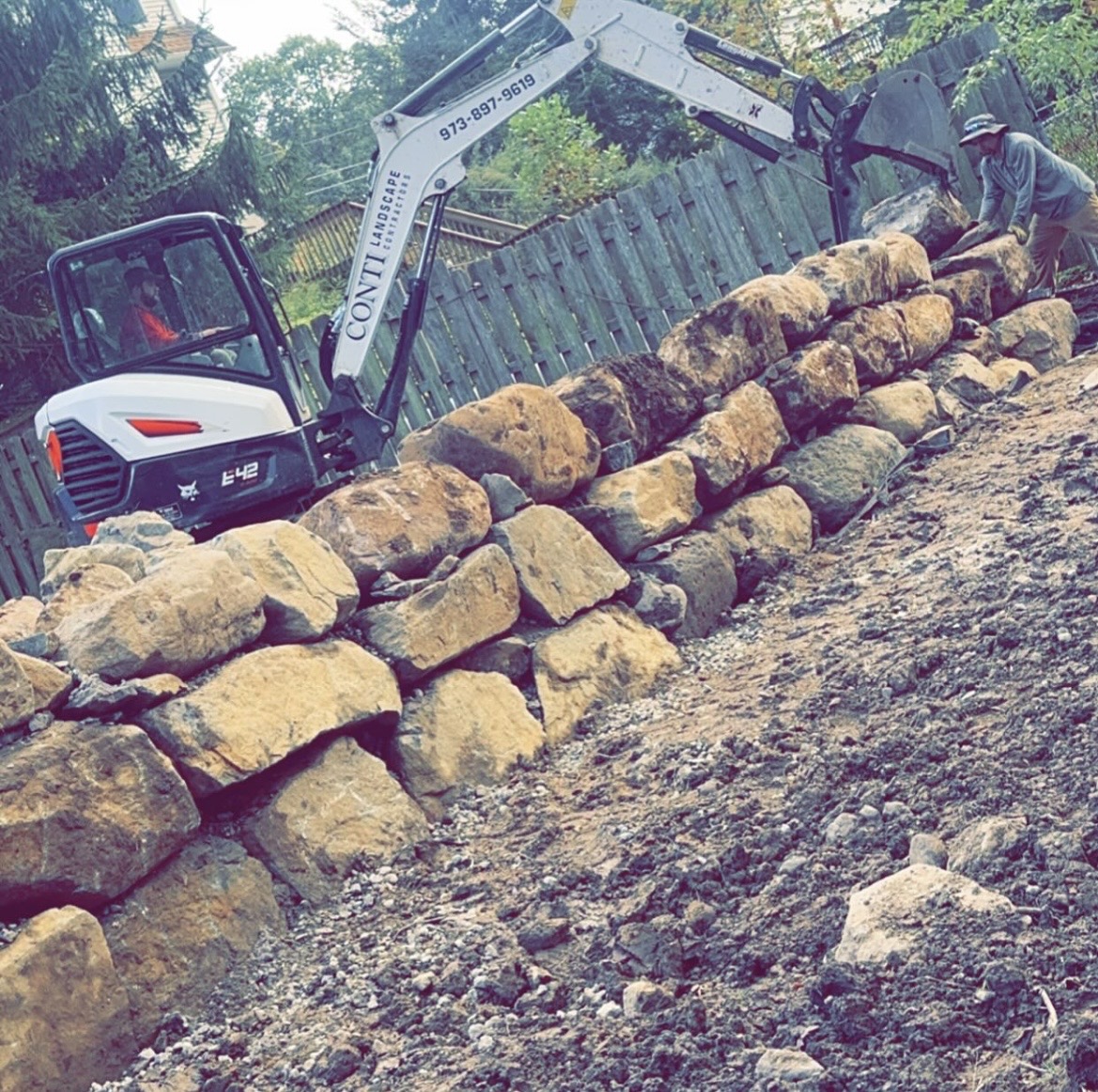 The Conti Landscape crew building a boulder retaining wall with their excavator